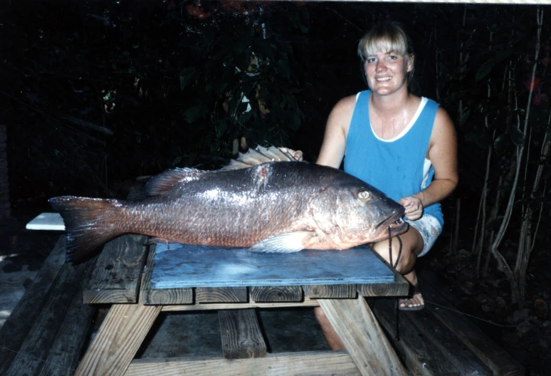 a lady is holding a big fish on a bench