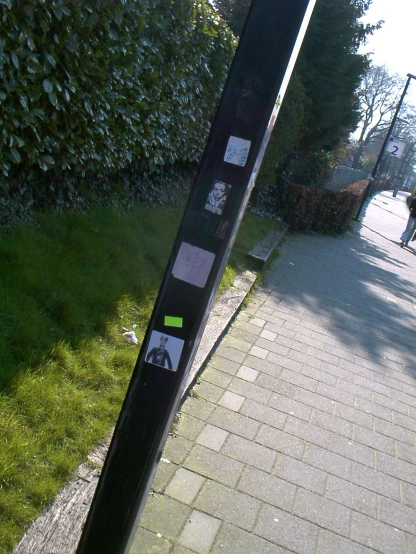 a pole on the side of a sidewalk with multiple stickers all over it