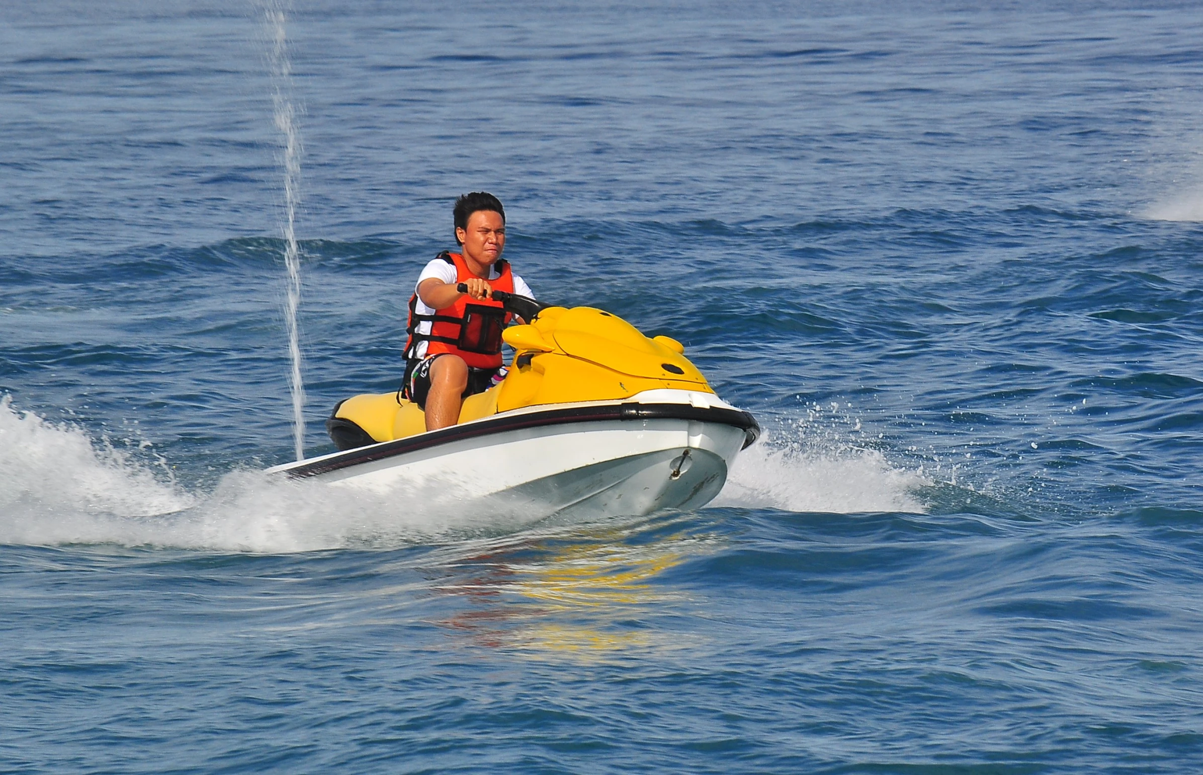 man in life jacket riding a yellow and black jet ski