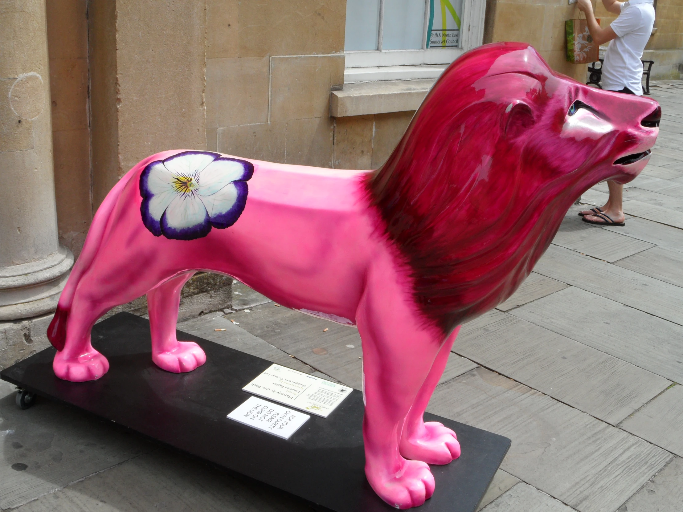 a pink lion statue on the sidewalk by a building