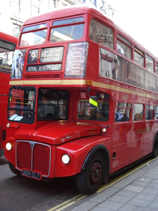 a red double decker bus driving past two other buses