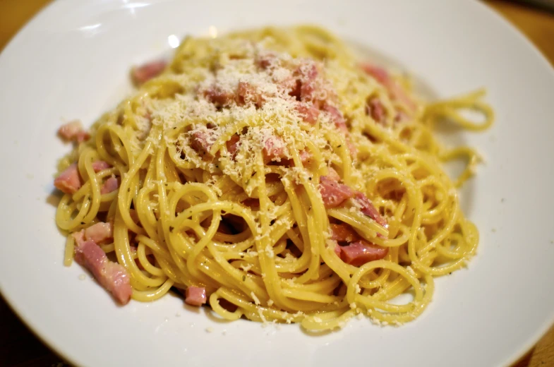 a white plate topped with pasta covered in sauce and ham