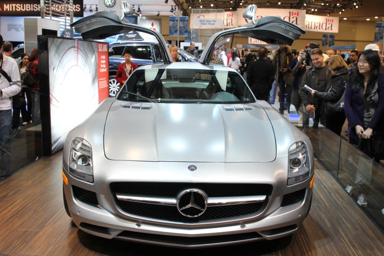 people stand and look at a silver sports car