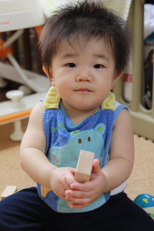 a toddler holding a small wood block while sitting on a floor