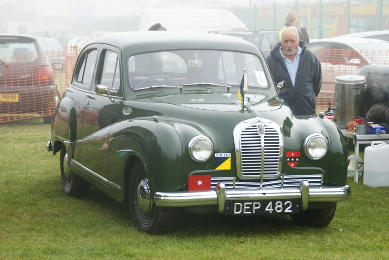 a man in a grey coat is standing by an antique car