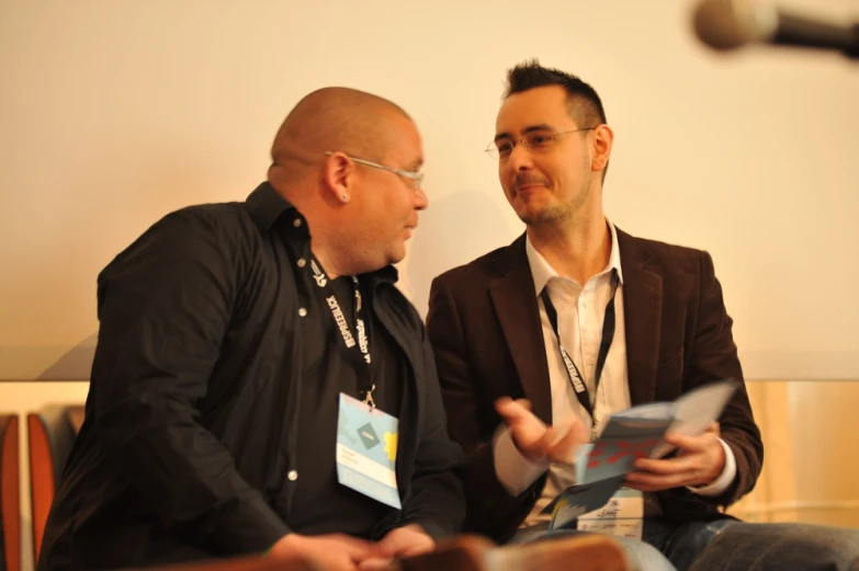 two men talking together while one holds a card