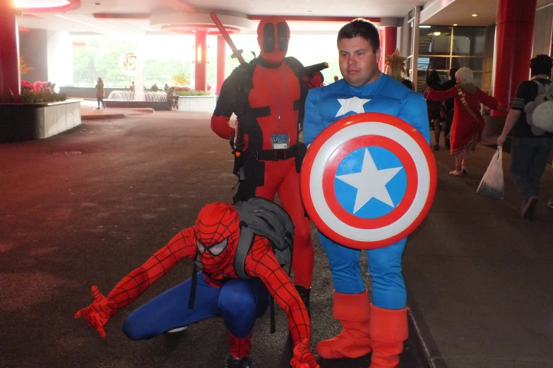 two people dressed as a spiderman and captain america stand next to each other in front of a hallway