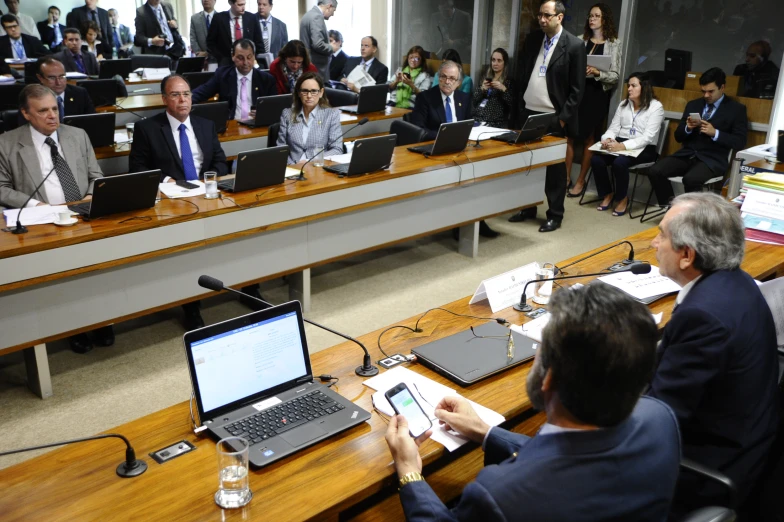 people are sitting at long wooden desks with laptop computers on them