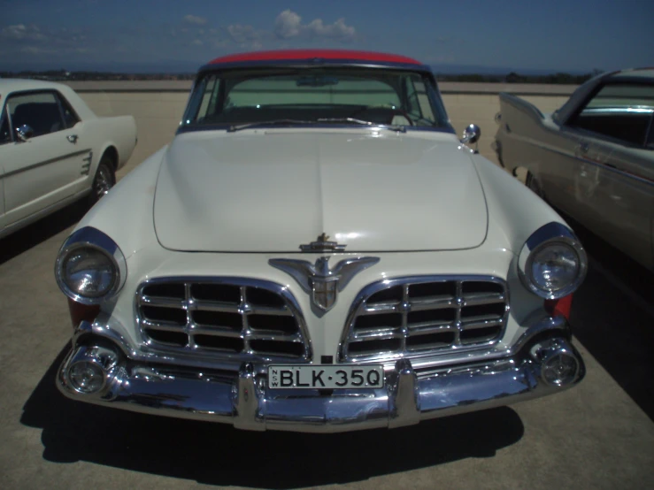 two older cars in a lot with a sky background