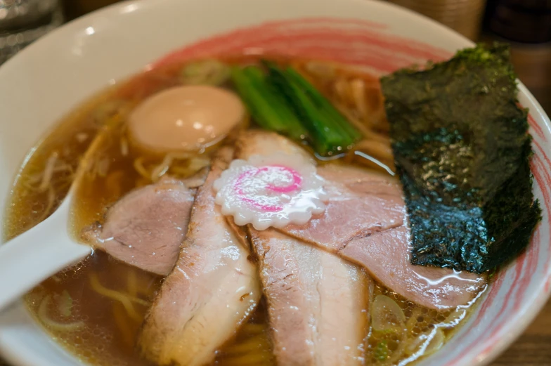 an asian soup with noodles and ham on a white plate