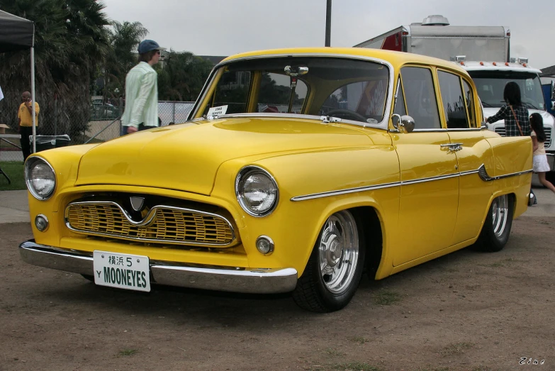 an old yellow car sitting in the parking lot