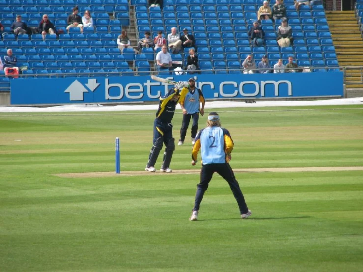 people standing on a grass field playing a game of cricket