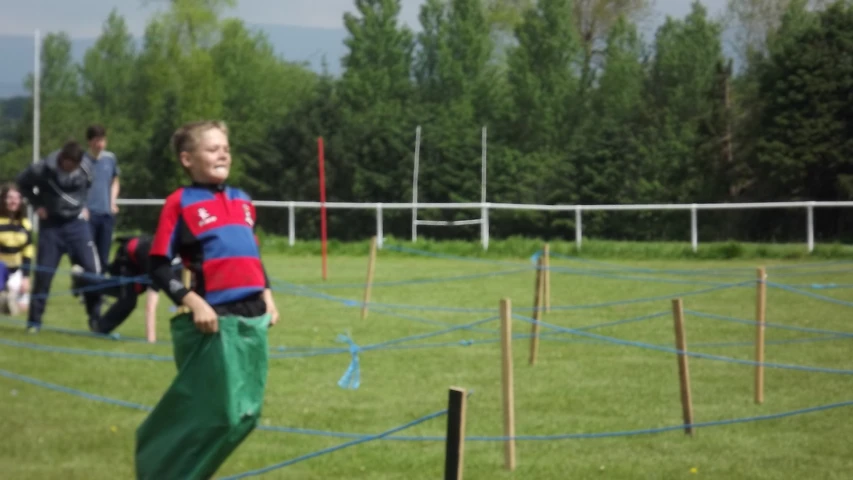 a little boy wearing green pants standing on top of a grass field