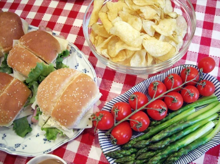 two plates of food and a bowl of chips on a checkered table cloth