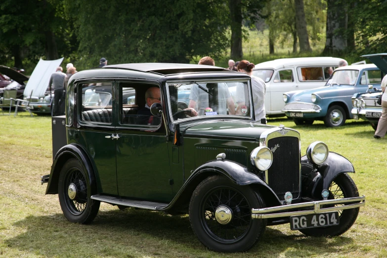 an old time black car is parked with people standing around