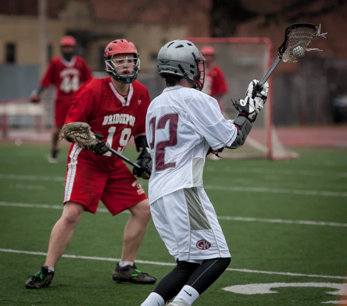 some s playing lacrosse with the ball and the goalie wearing red