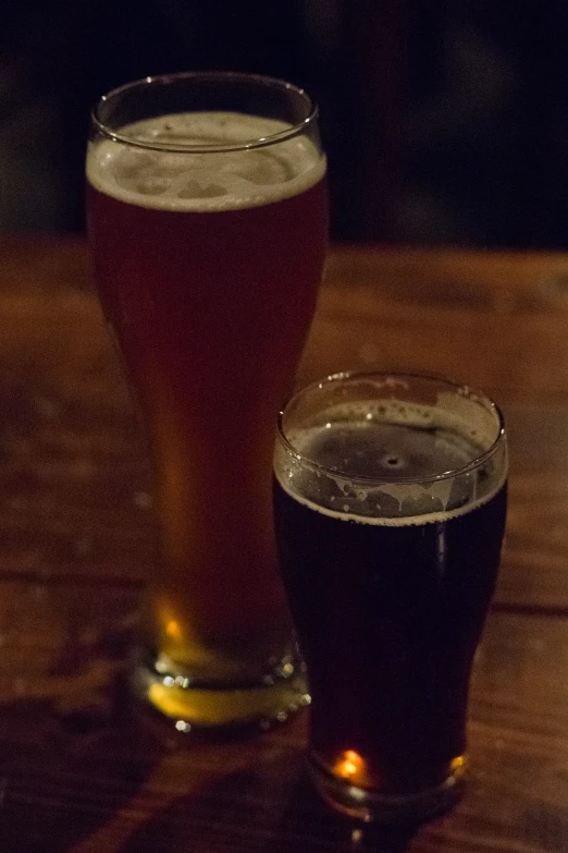 two glasses of beer sitting on a wooden table
