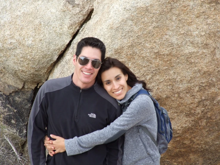 a man and woman standing next to each other by a rock