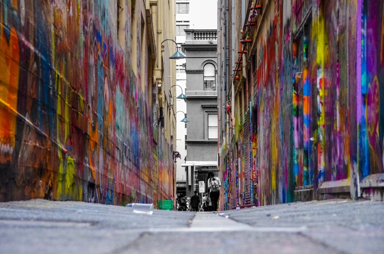 a narrow alley with colorful painted walls, a person walking down one end and another man with an umbrella in the distance