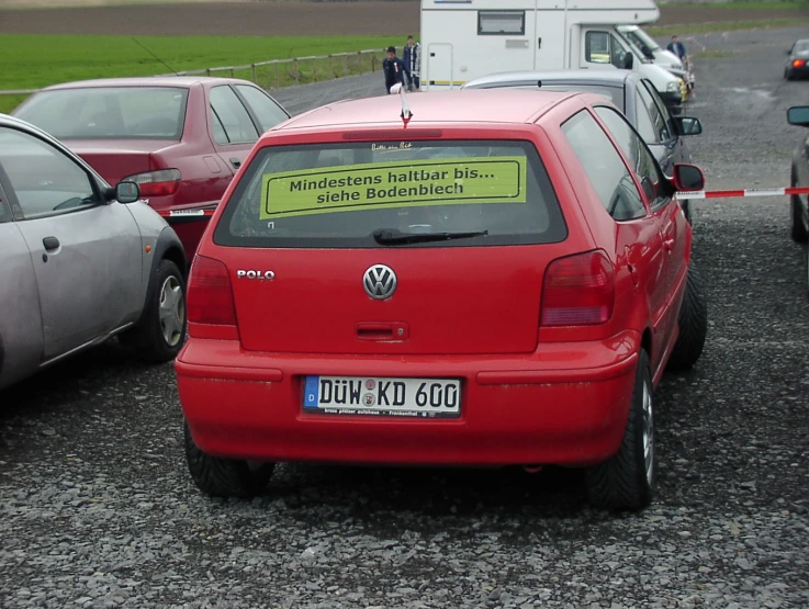 red volkswagen car with sign taped to the back sitting on gravel