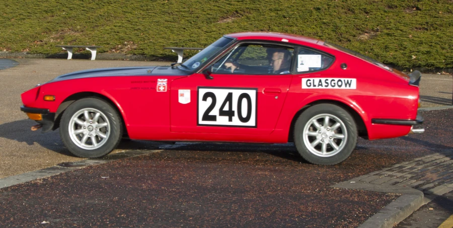 the front of a red car, with a black top, and a sign reading 240