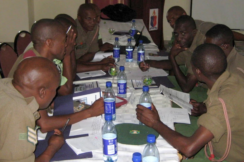 six men sitting at a large table with water bottles on it