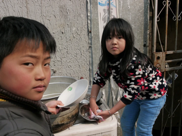 the young children are washing dishes in a basin