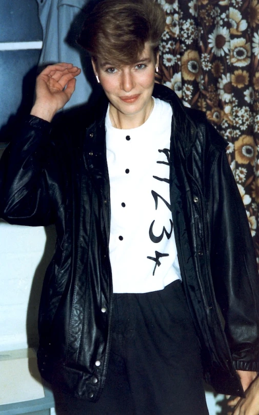 a young man in a jacket and t - shirt with his fingers near his head