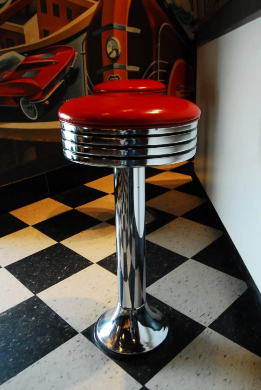 a red stool sitting on top of a black and white checkered floor