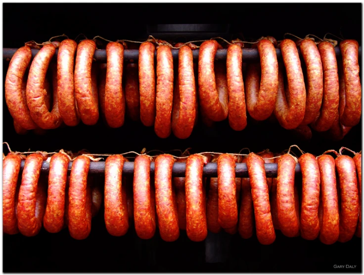 three rows of uncooked sausages being hung up on a grill