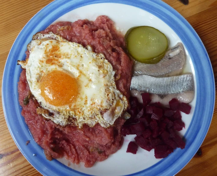 a white plate topped with meat, an egg and pickles