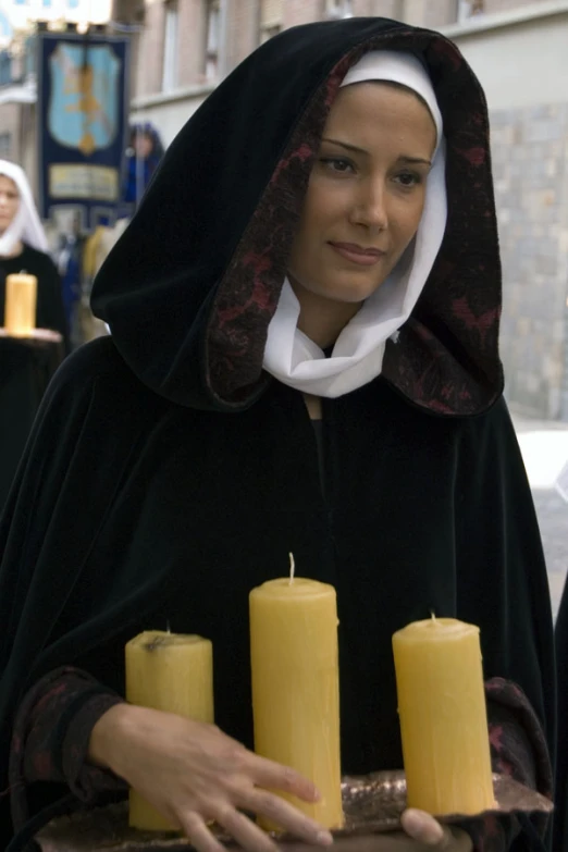 the nun is holding a tray with three candles