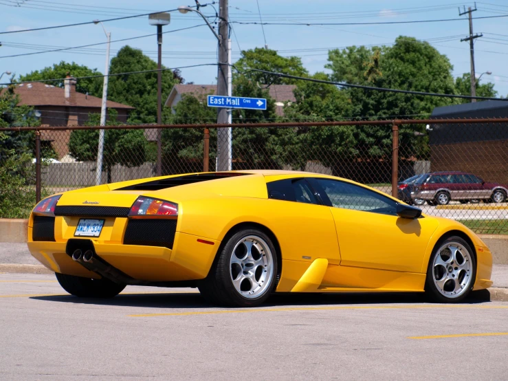 a yellow sport car parked in front of a fence