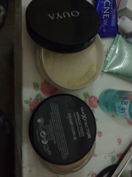 the contents of a make up kit including a powder jar and an earbud laying on top of a bed