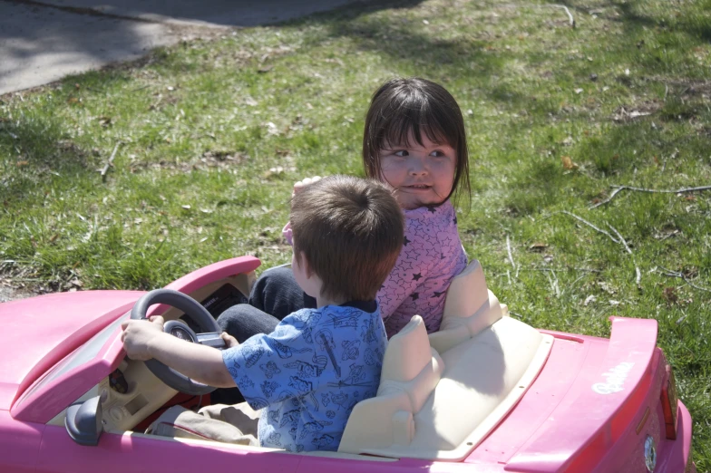 a little girl is sitting in a toy car and playing with another 