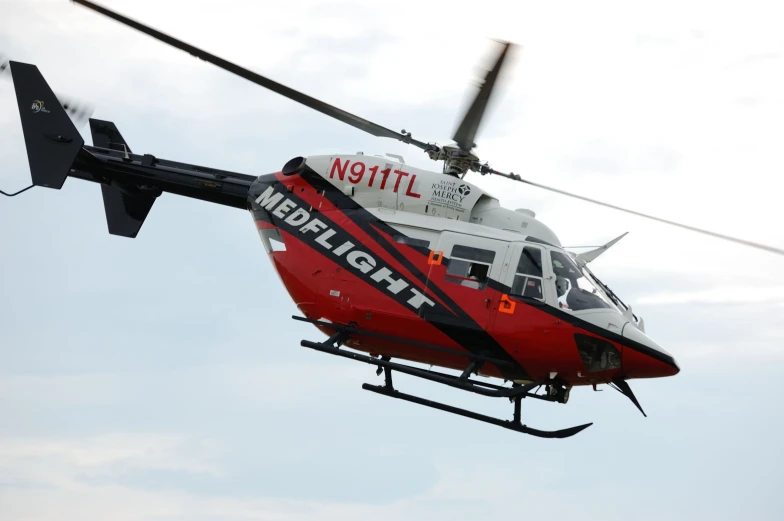 a red helicopter flying through the air on a cloudy day