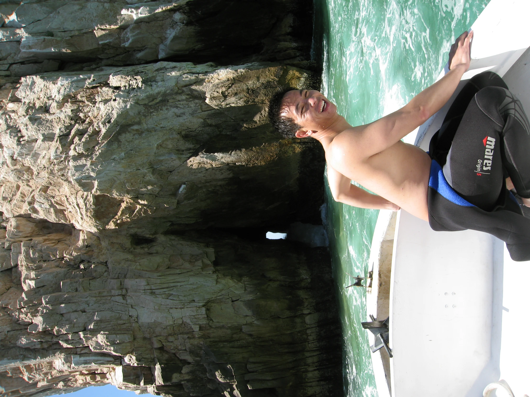 a shirtless man sits in the back of a boat in the water