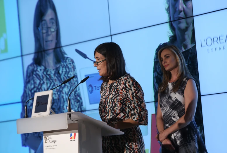 two women standing at podiums in front of a projection screen