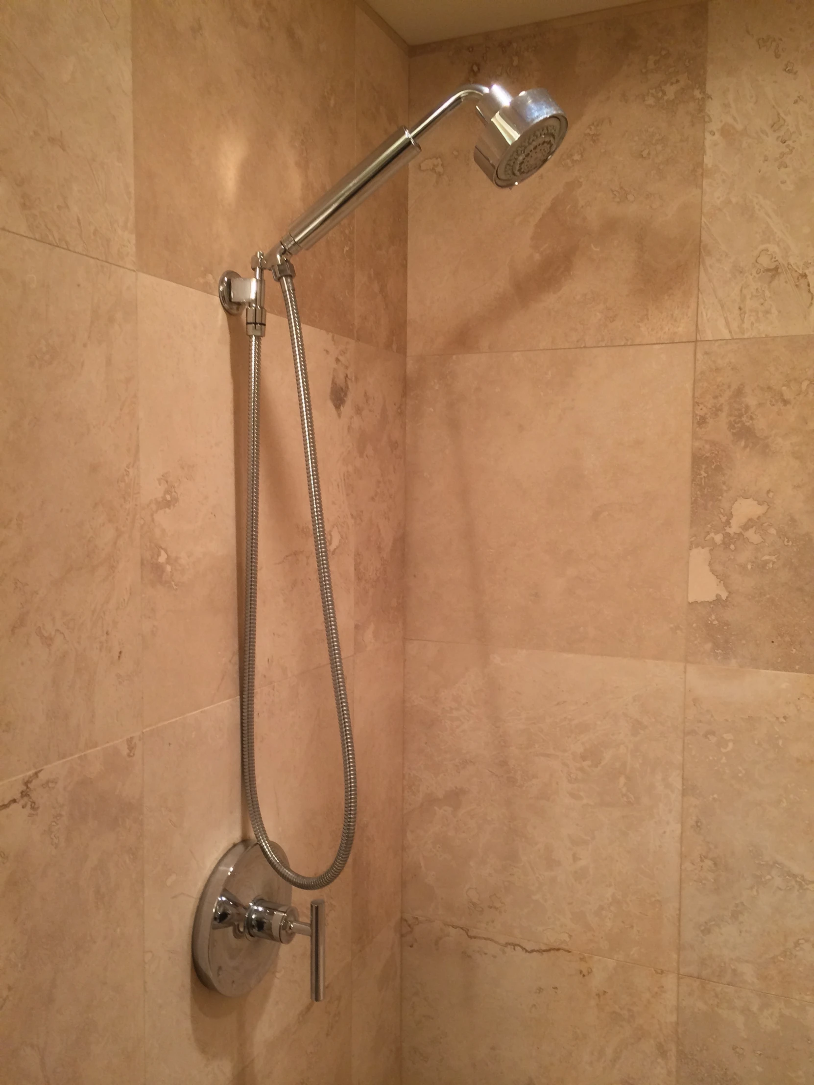 a shower head with a showerpipe on it and tan tiles