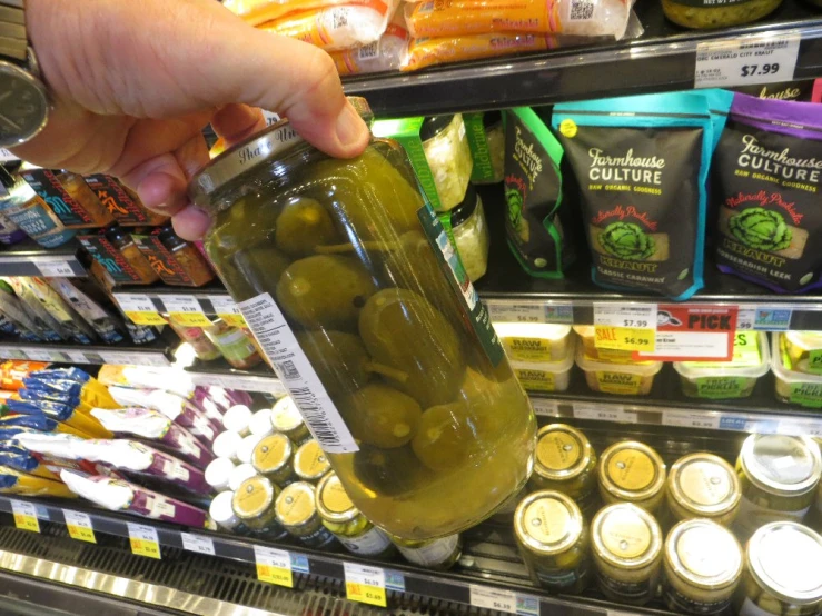 someone grabbing an item from the jar filled with green olives