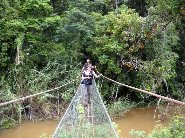 a woman standing on a wooden suspension bridge in the forest