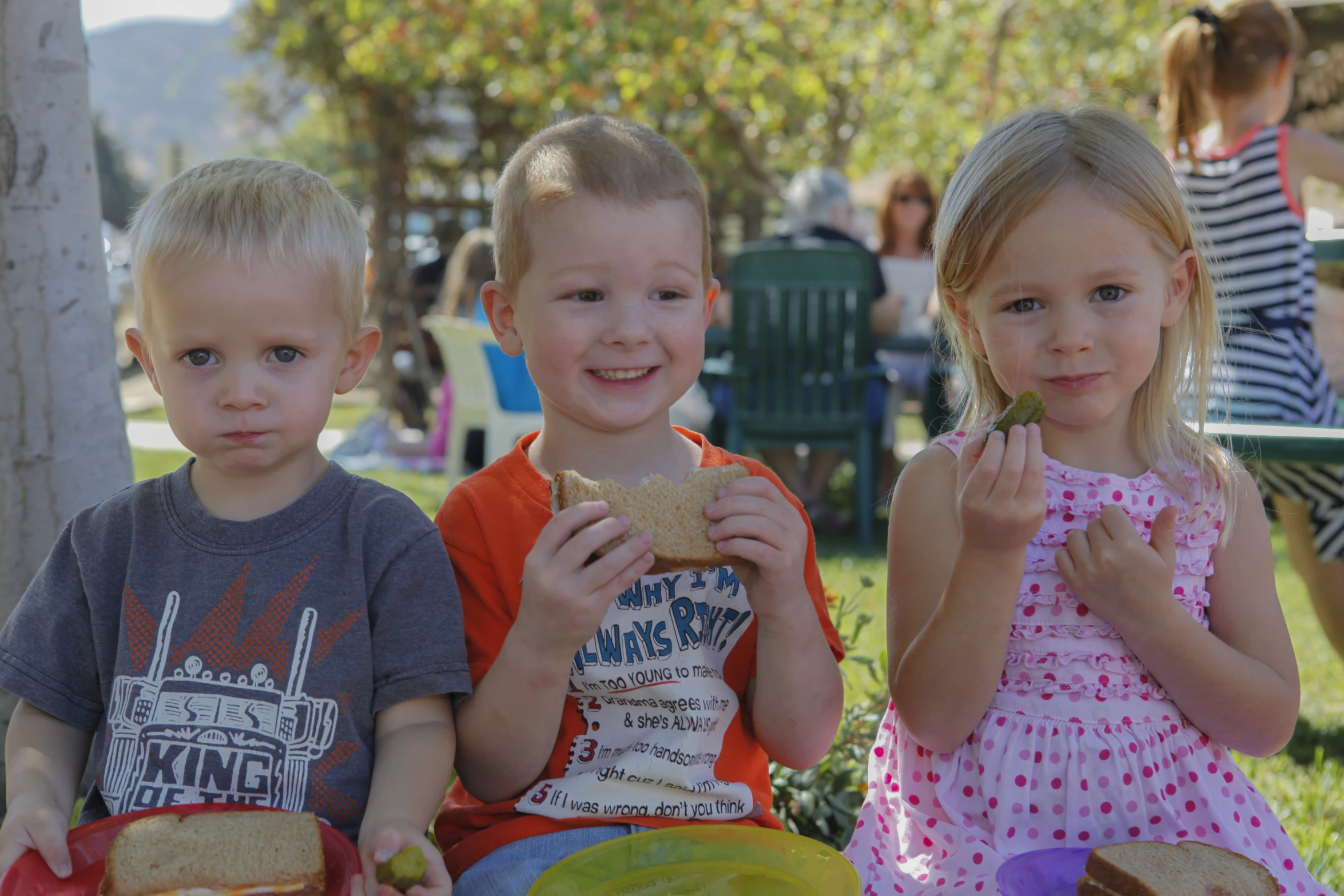 three children eating some food on some grass