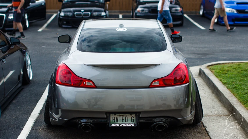 a silver car is parked in a parking lot with people walking and sitting near by