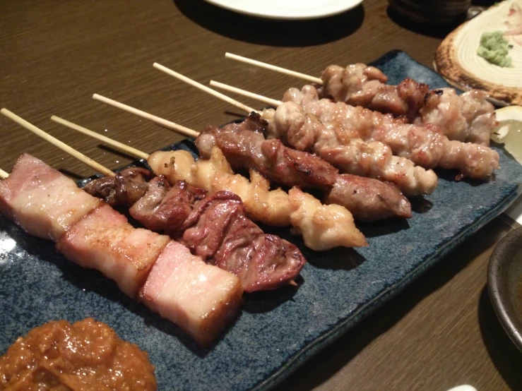 a dark blue tray holding skewers of meat with chopsticks on it