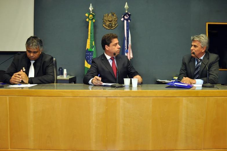 three men sitting at a table discussing and writing