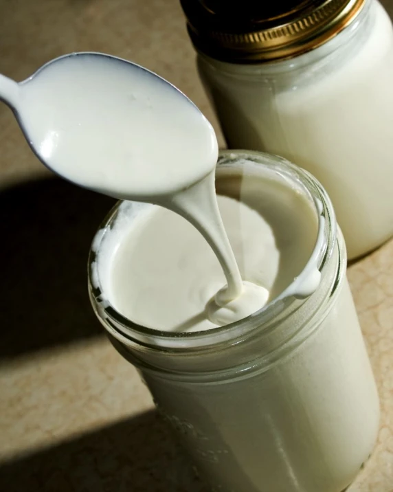 a glass jar with yogurt being poured