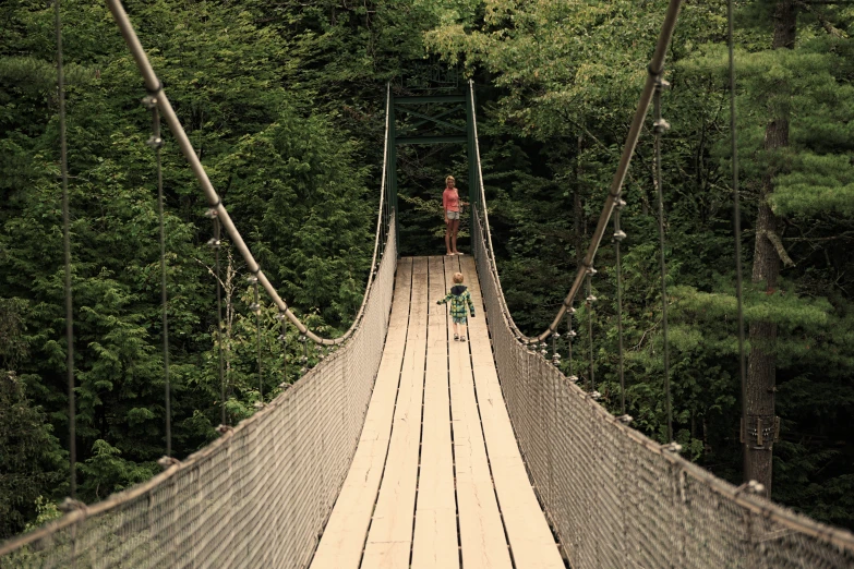 a woman walks across a suspended bridge in the woods