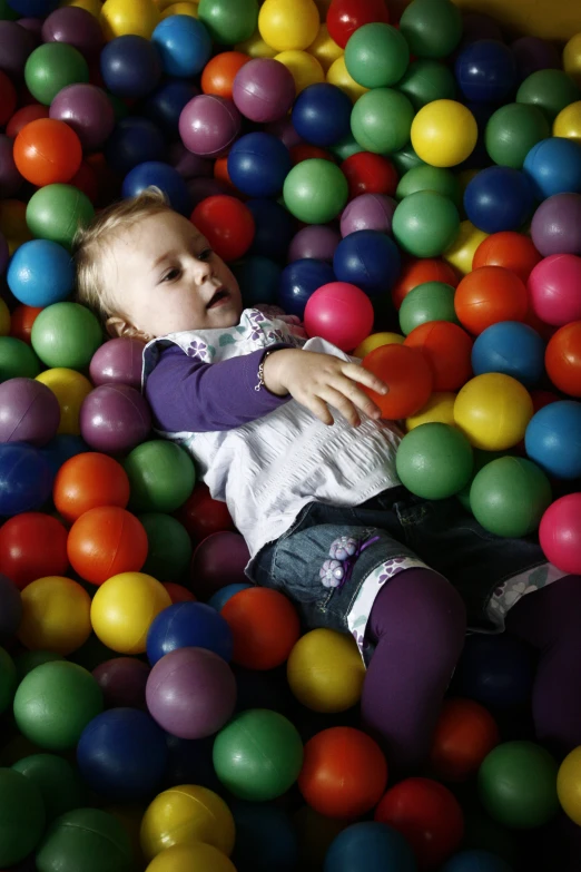 small child laying in ball pit with purple and white legging