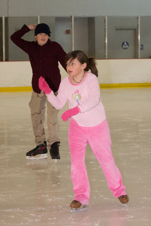 two children skate on an ice rink while one child holds a hand out