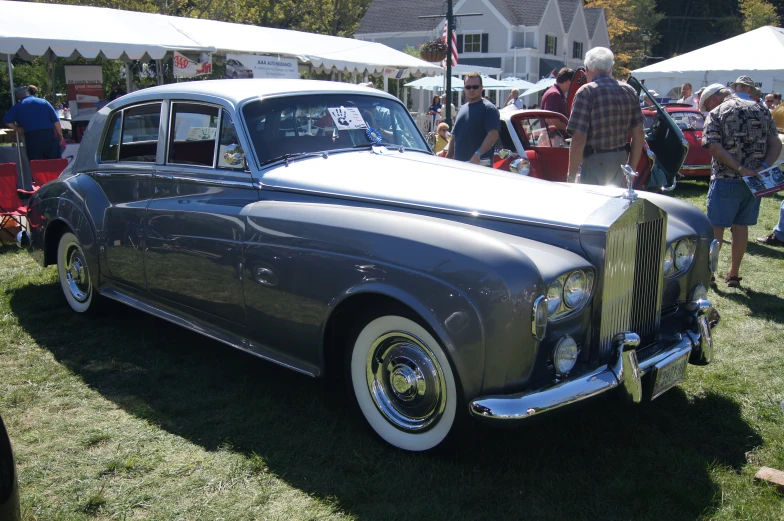 a silver car with people looking at it on a field